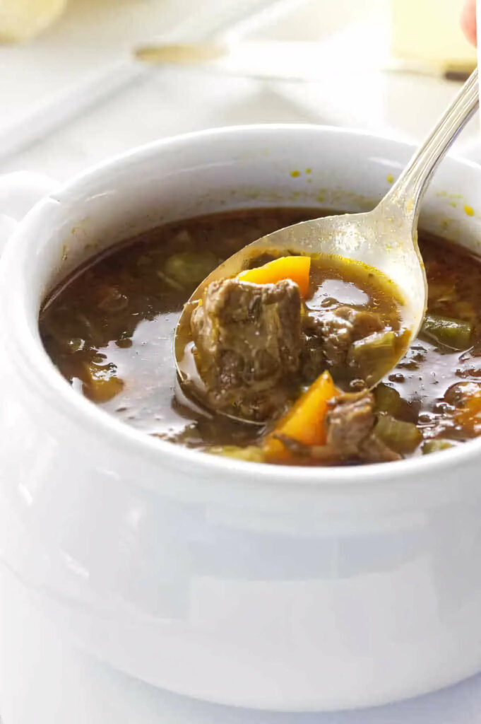 A spoon in a bowl of homemade beef soup with veggies.