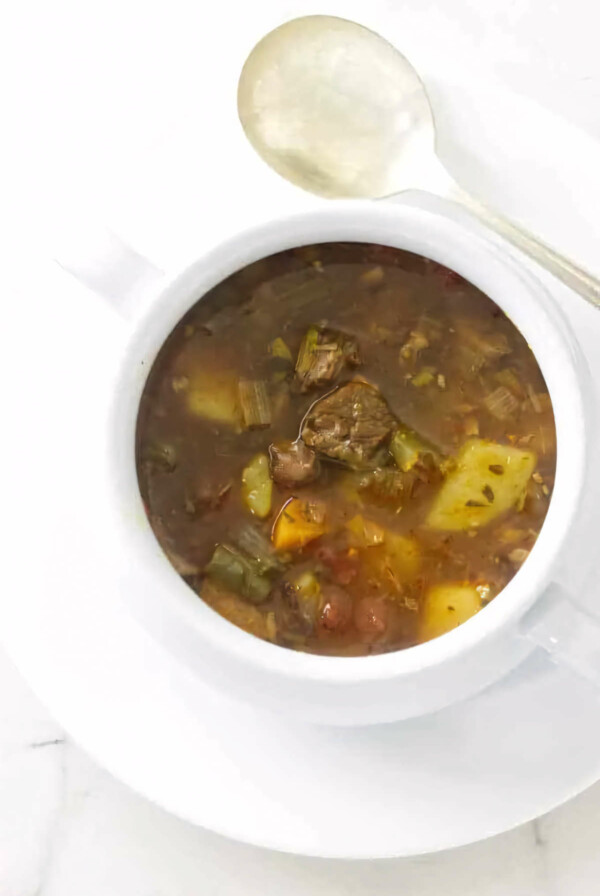 A bowl of vegetable beef soup next to a spoon.