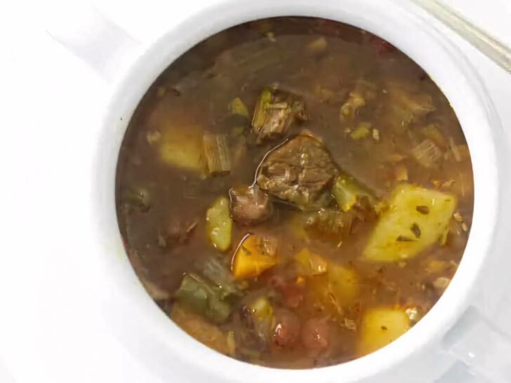 A bowl of vegetable beef soup next to a spoon.