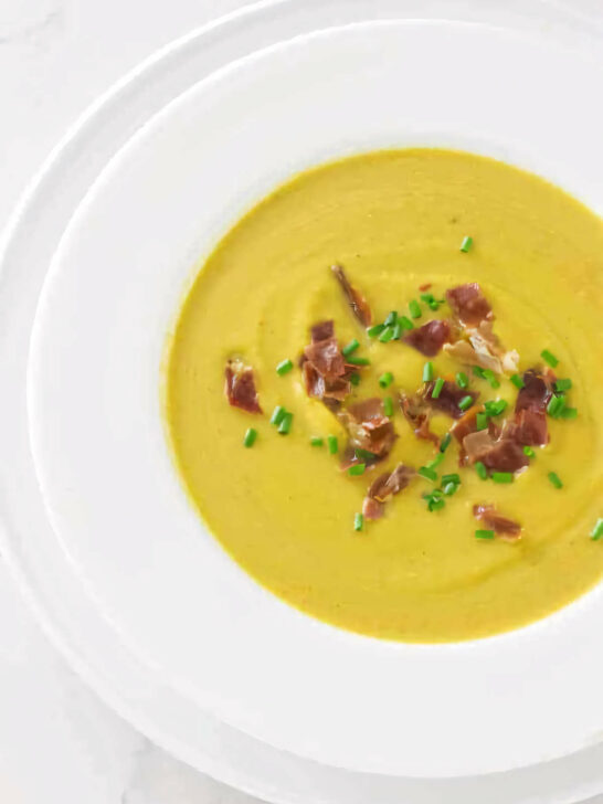 A soup bowl filled with butternut squash soup and garnished with chives and prosciutto.