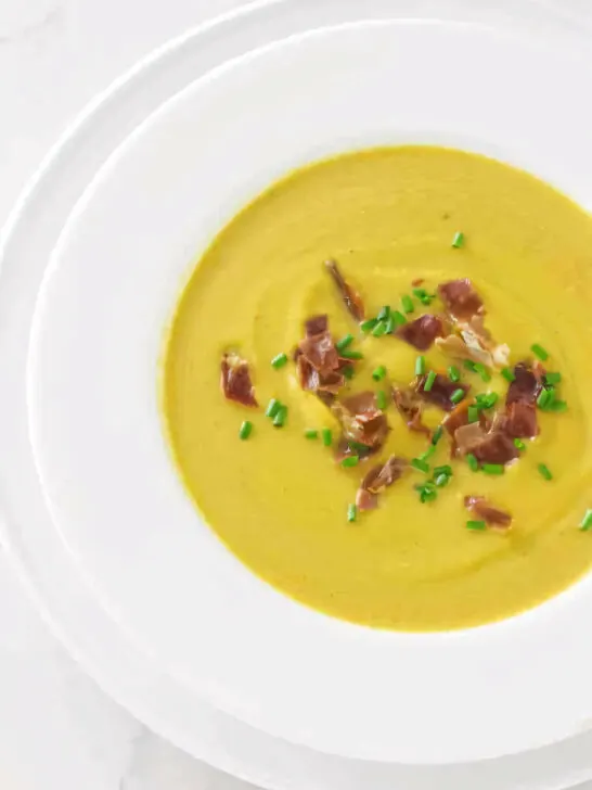 A soup bowl filled with butternut squash soup and garnished with chives and prosciutto.