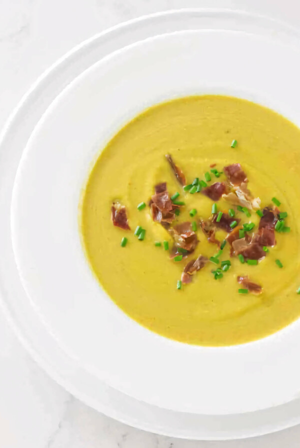 A soup bowl filled with butternut squash soup and garnished with chives and prosciutto.