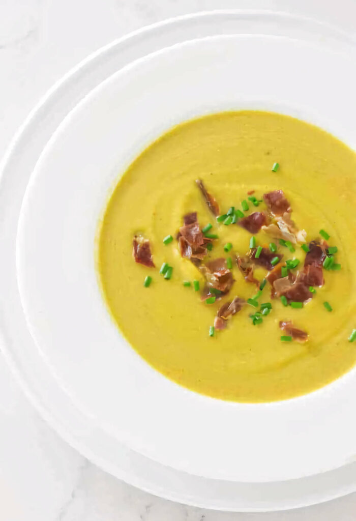 A soup bowl filled with butternut squash soup and garnished with chives and prosciutto.