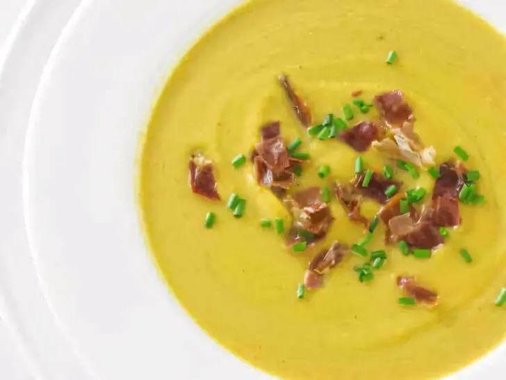 A soup bowl filled with butternut squash soup and garnished with chives and prosciutto.