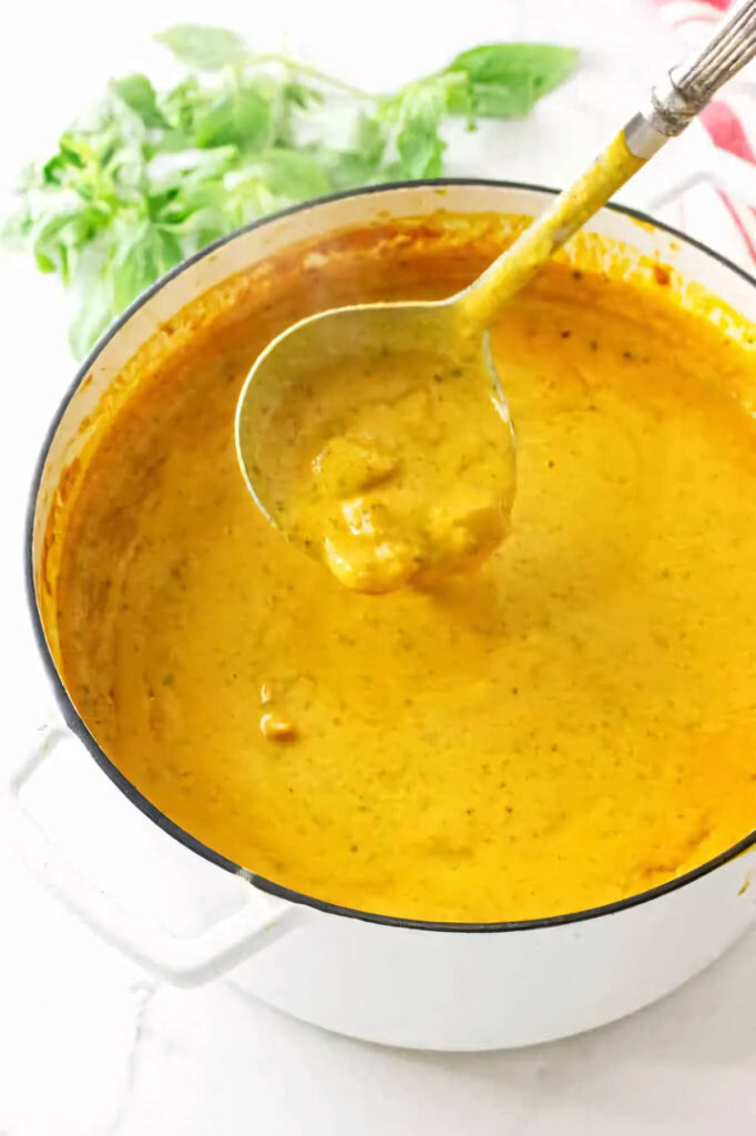 A ladle scooping some creamy tomato soup from a Dutch oven.