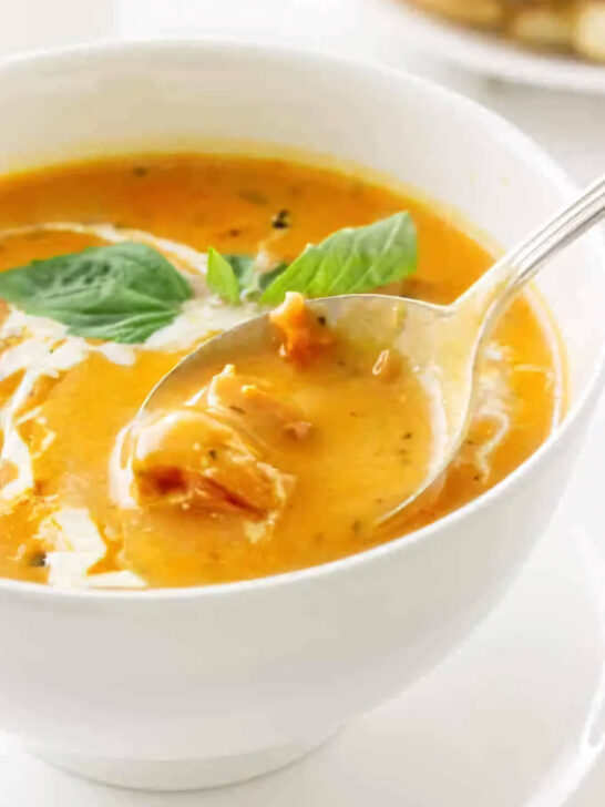 A spoon scooping some tomato soup from a bowl.