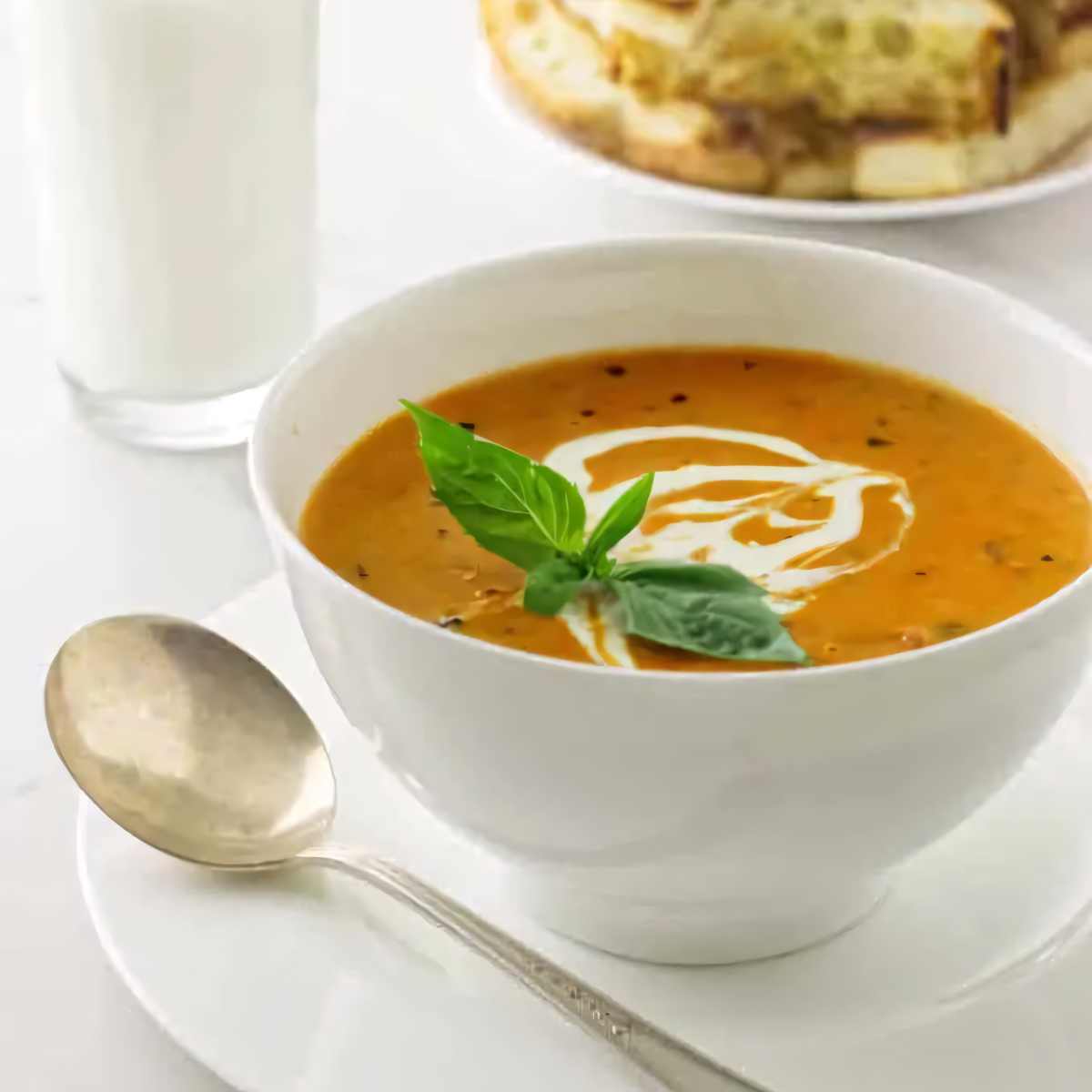 A bowl of roasted tomato garlic soup with a sprig of basil on top.