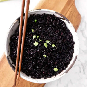 A bowl of black rice with chopsticks on top.