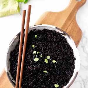 A serving bowl filled with black rice and garnished with basil.