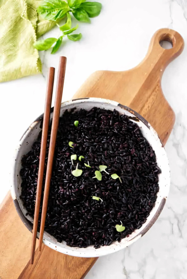 A serving bowl filled with black rice and garnished with basil.