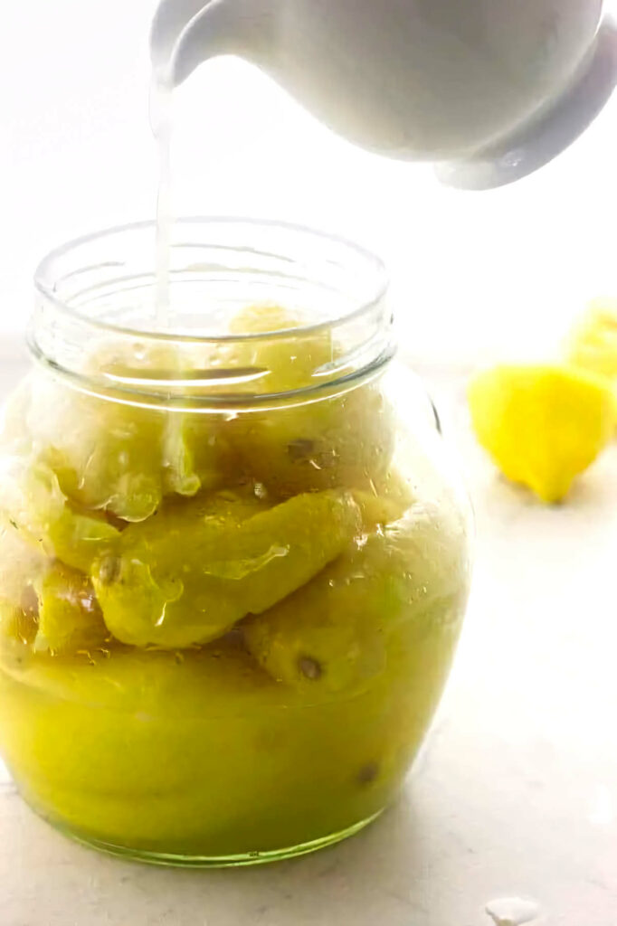 Pouring lemon juice in a jar filled with salted lemons.