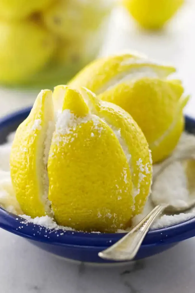 Two lemons in a dish of salt with a spoon sitting beside them.