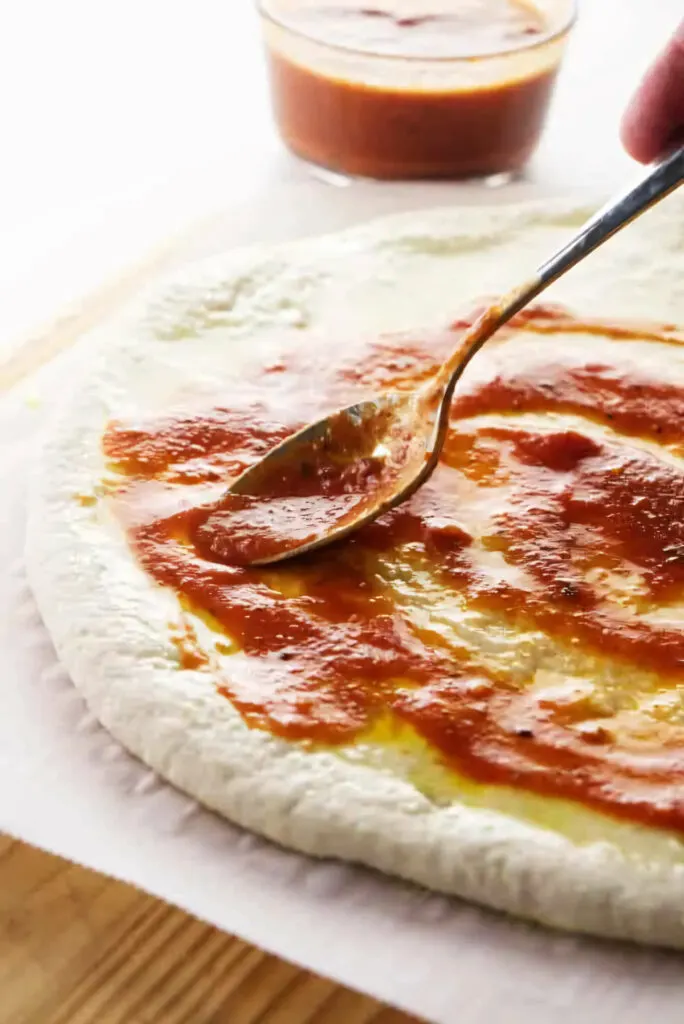 Spreading pizza sauce on the shaped dough.