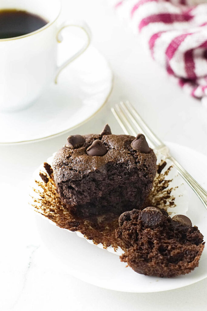 A small plate with a muffin in front of a cup of coffee.