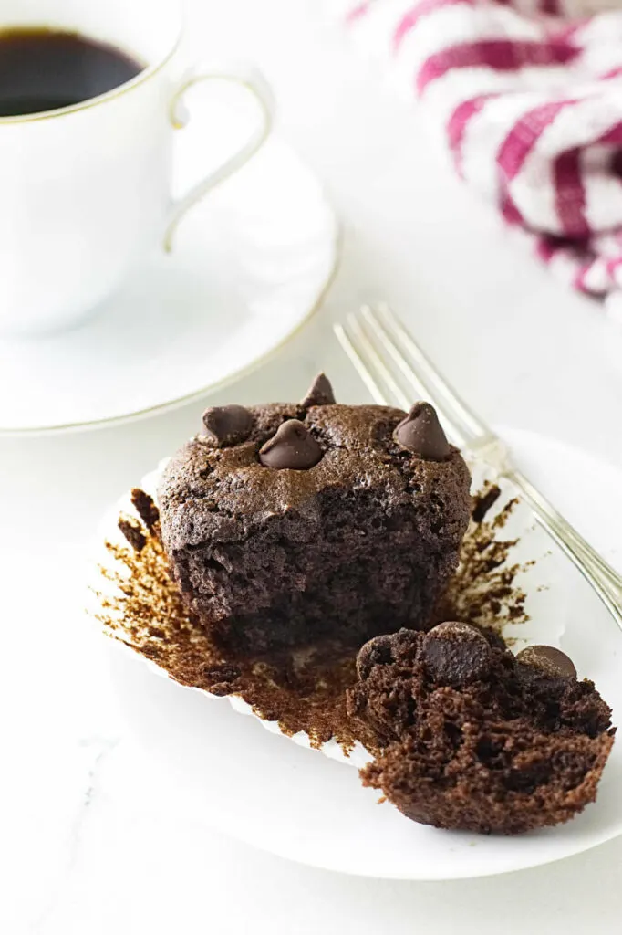 A small plate with a muffin in front of a cup of coffee.