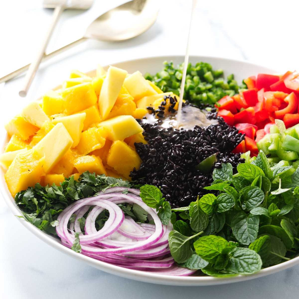 Pouring vinaigrette on a black rice and mango salad.