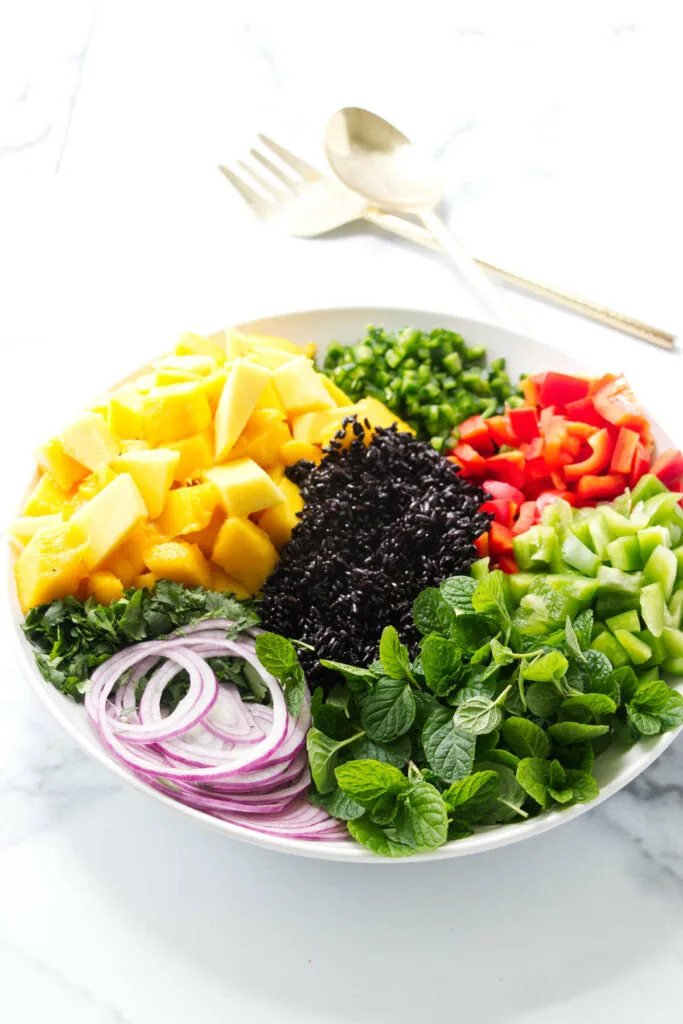 A large bowl filled with mango and black rice salad ingredients.