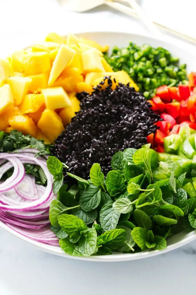 A serving bowl filled with black rice, mango, and herbs and veggies.