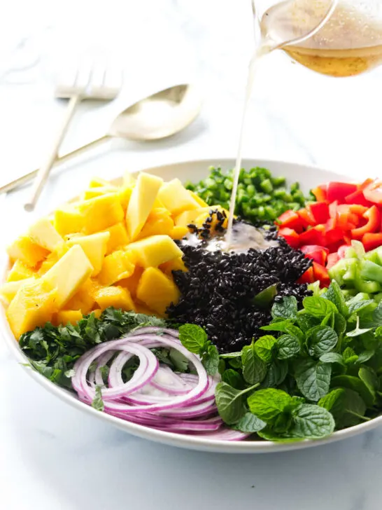 Pouring vinaigrette on a salad with black rice and mango.