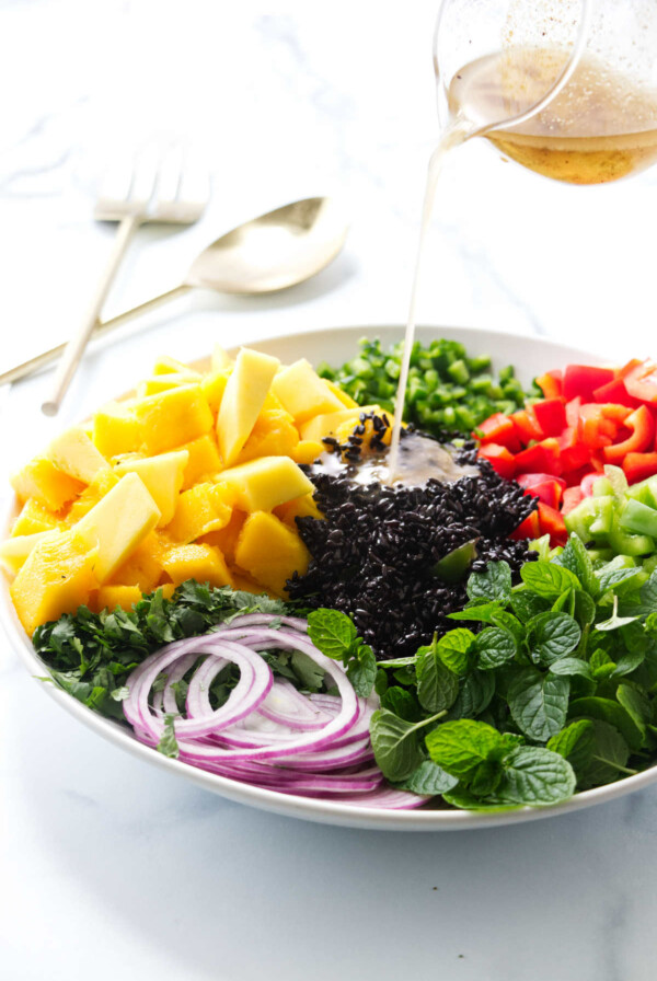 Pouring vinaigrette on a salad with black rice and mango.