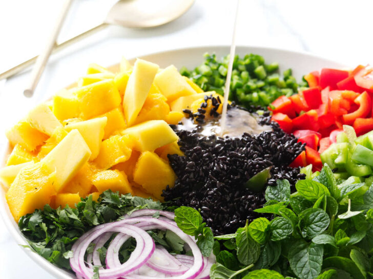 Pouring vinaigrette on a salad with black rice and mango.