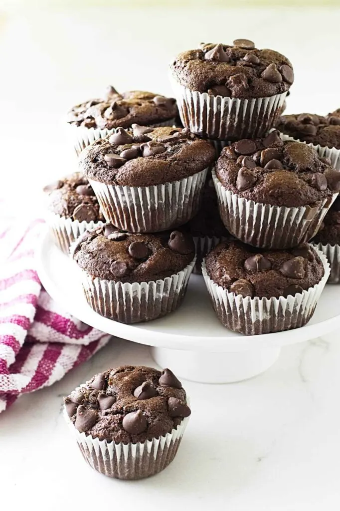 A platter of chocolate einkorn muffins next to a white and red towel.