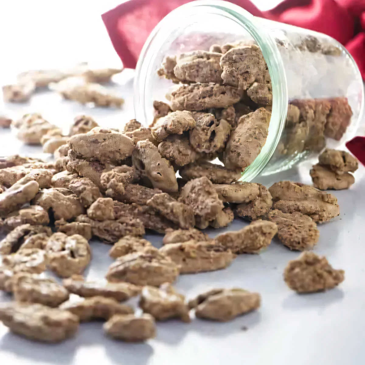 Candied pecans spilling out of a jar that is laying on its side.