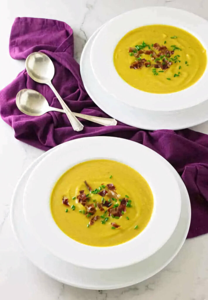 Two bowls of butternut squash soup with prosciutto on top.