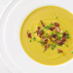 A bowl of butternut squash soup topped with prosciutto and chives.