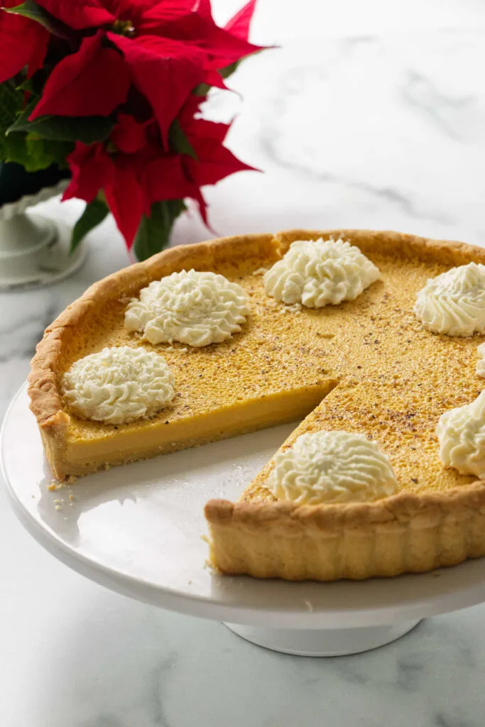 An eggnog custard tart on a serving platter with one slice removed.