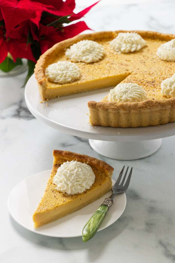 A slice of an eggnog cream tart next to a platter with a whole tart.