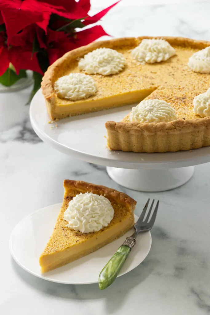 A slice of an eggnog cream tart next to a platter with a whole tart.