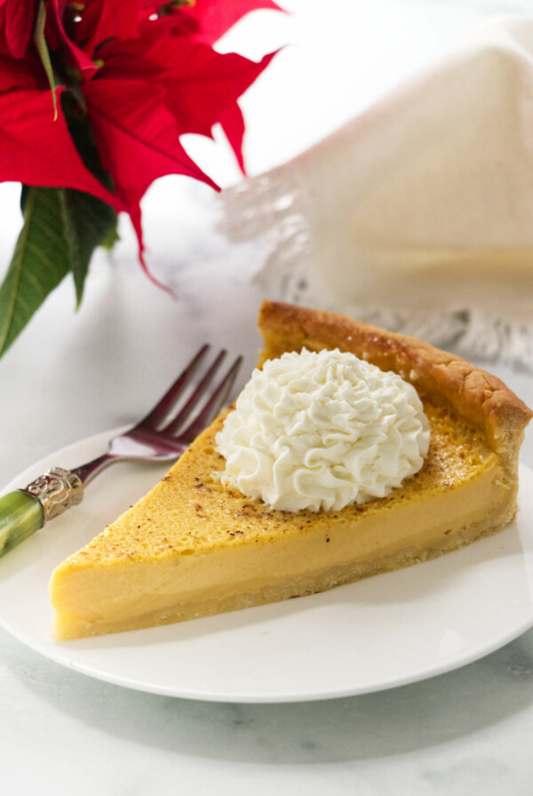 A slice of an eggnog tart next to a poinsettia.