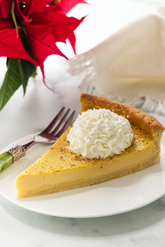 A slice of an eggnog tart next to a poinsettia.