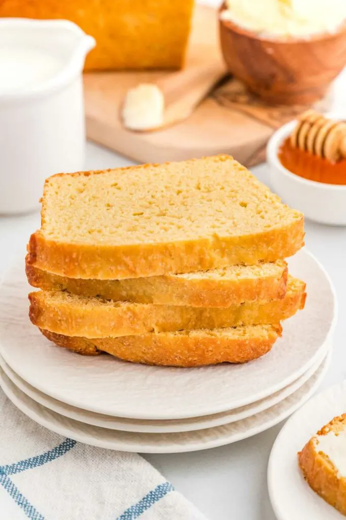 Four slices of einkorn sandwich bread stacked on a plate with butter in the background.