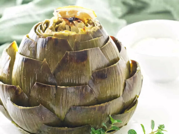 A roasted artichoke on a plate with a sprig of thyme.