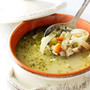 A ladle scooping noodle soup out of a pot.