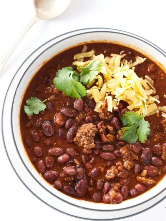 A bowl filled with beef chili beans next to a spoon.