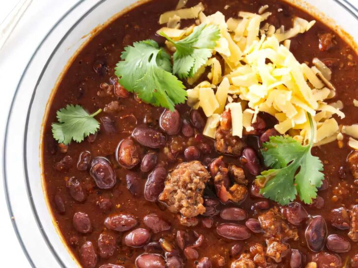 A bowl filled with beef chili beans next to a spoon.