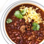 A bowl of chili beans topped with cheddar cheese and parsley.