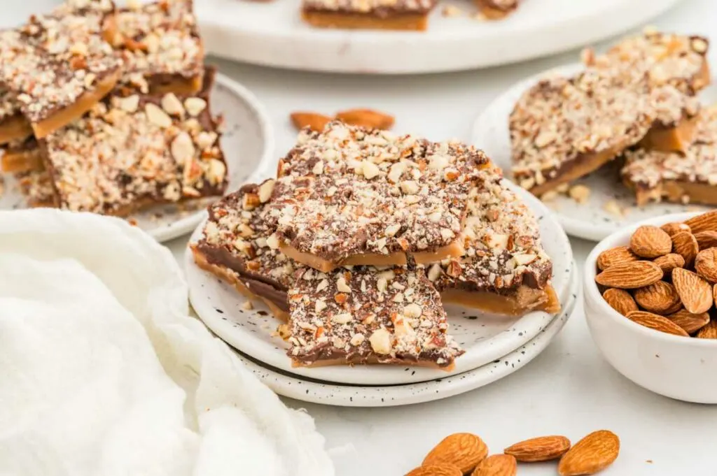 Several plates filled with English toffee candy next to a bowl of almonds.