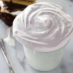 A jar filled with marshmallow cream next to a spoon.