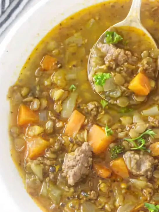 A spoon in a bowl of sausage lentil soup.