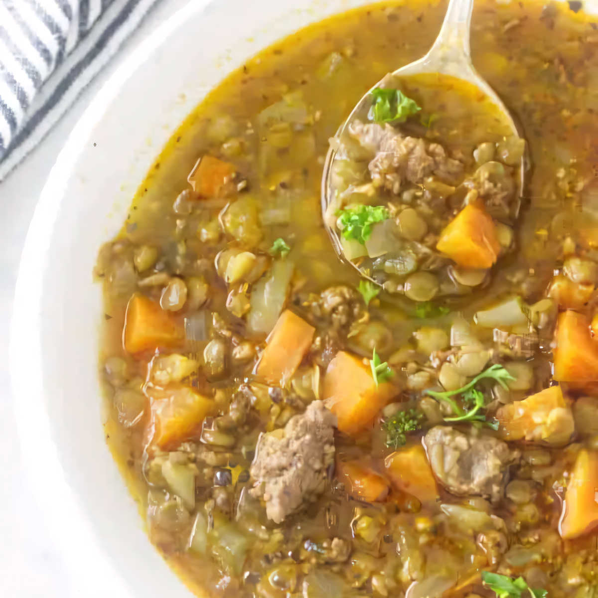 A spoon in a bowl of sausage lentil soup.