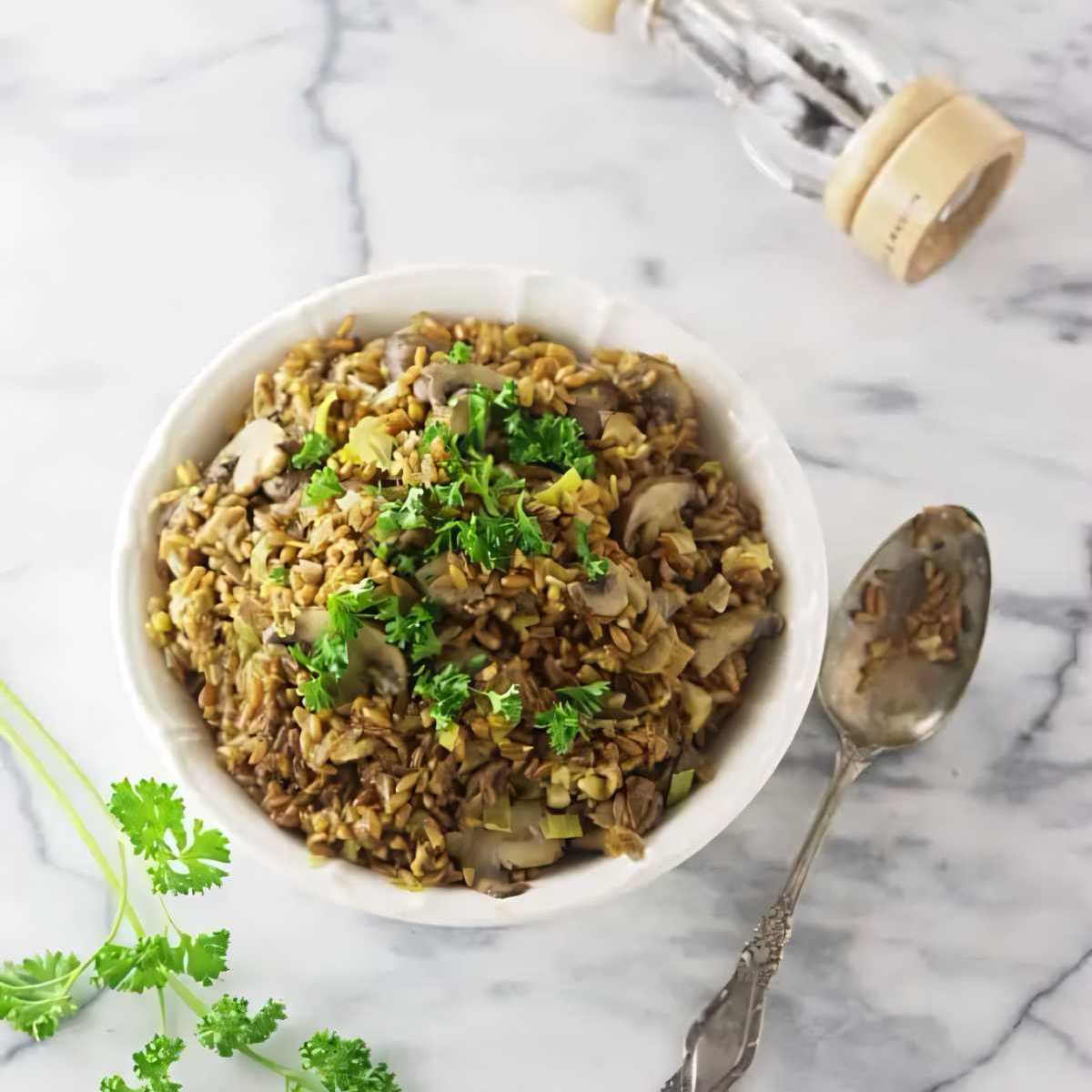 A bowl filled with mushroom farro risotto next to a spoon.