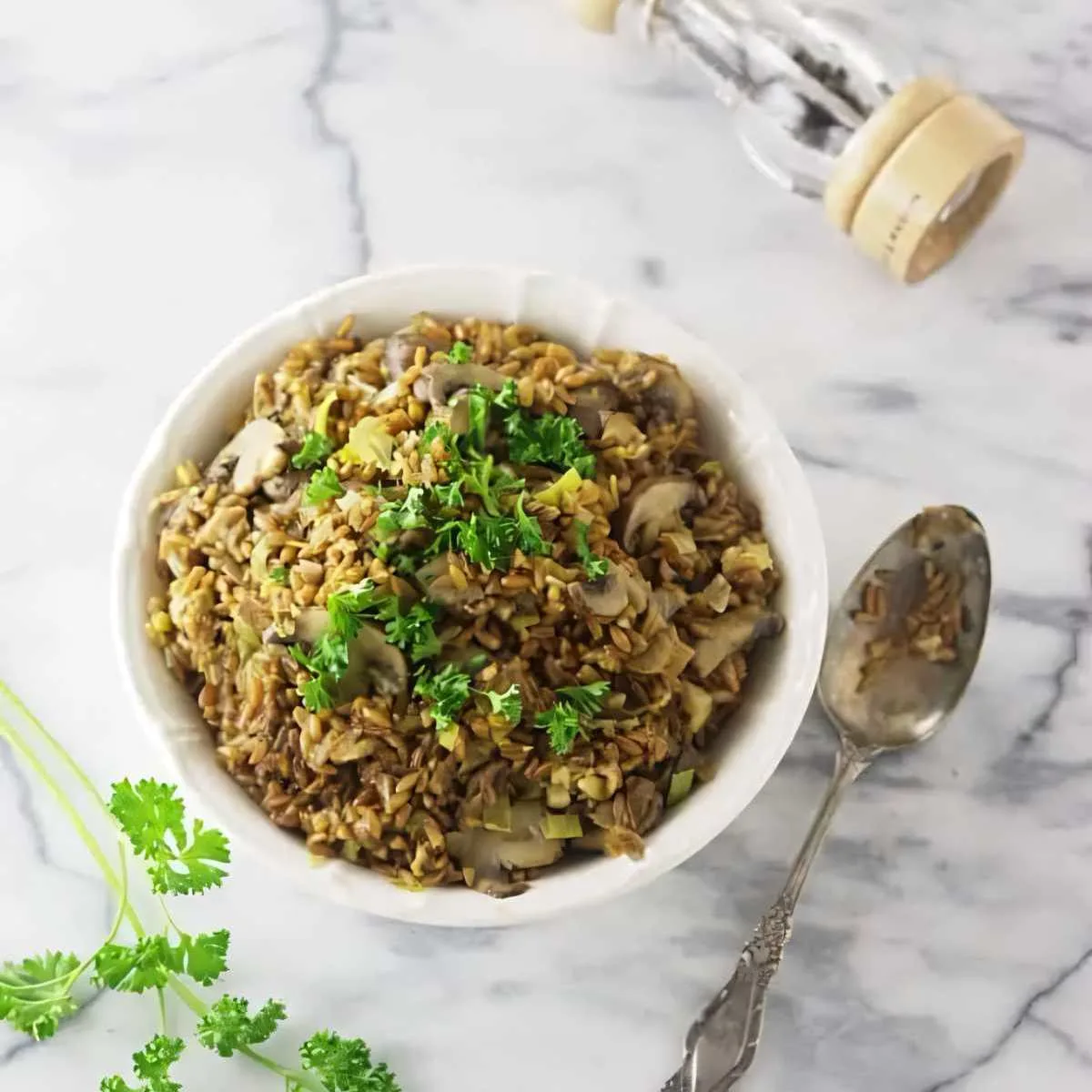 A bowl filled with mushroom farro risotto next to a spoon.