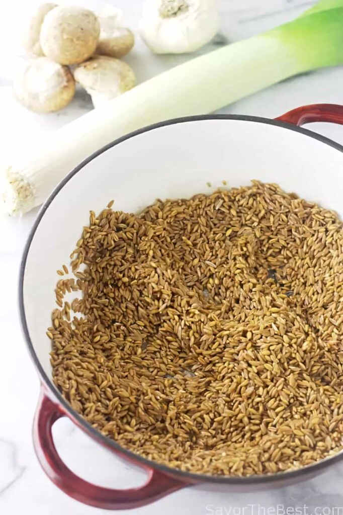 Farro grains in a pot next to mushrooms and a leek.