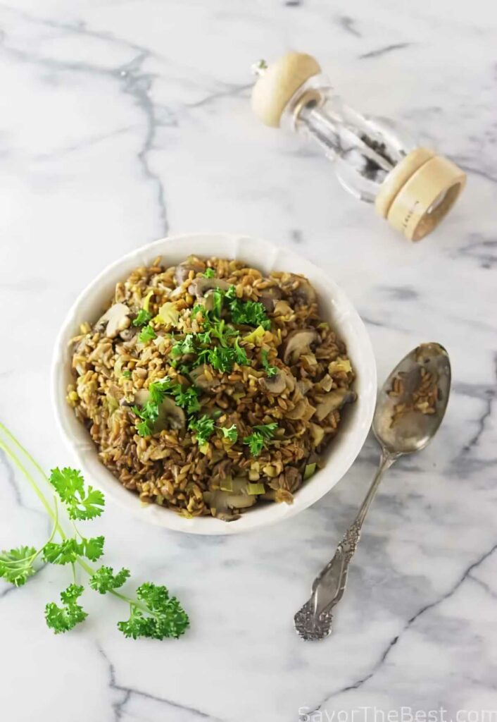 Mushroom farro risotto in a bowl next to a spoon and a pepper mill.