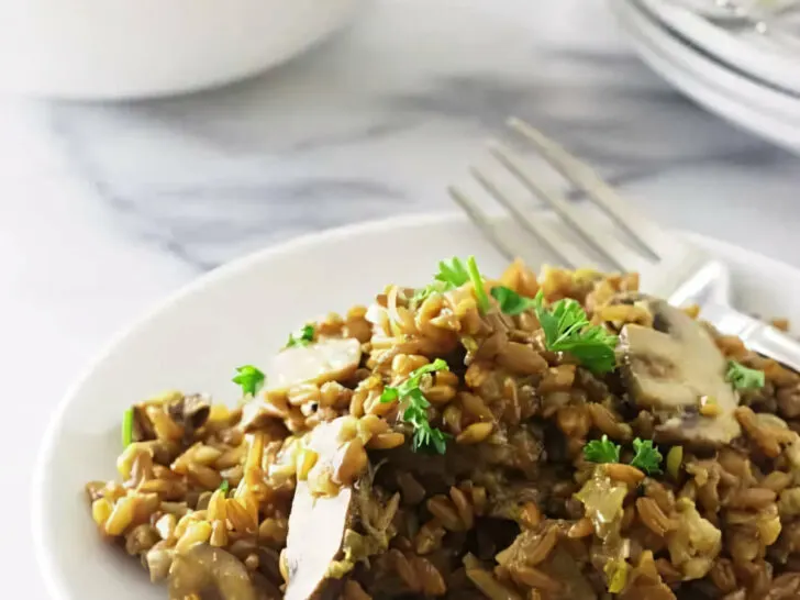 A plate with a serving of creamy mushroom farrotto next to a fork.