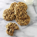 Spelt oatmeal raisin cookies on a counter with milk.